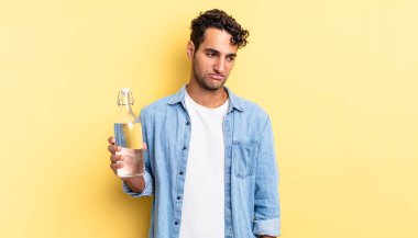 Hispanik yakışıklı adam üzgün, üzgün ya da kızgın hissediyor ve yana bakıyor. su şişesi kavramı