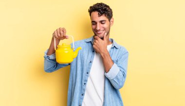 Mutlu, kendine güvenen, elleri çenesinde gülümseyen İspanyol yakışıklı bir adam. çaydanlık konsepti