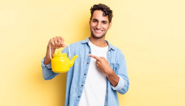 İspanyol yakışıklı adam neşeyle gülümsüyor, mutlu hissediyor ve bir tarafı işaret ediyor. çaydanlık konsepti