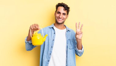 İspanyol yakışıklı adam gülümsüyor ve arkadaş canlısı görünüyor, üç numarayı gösteriyor. çaydanlık konsepti