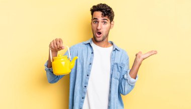 İspanyol yakışıklı adam şaşırmış ve şok olmuş görünüyor. Çenesi düşmüş ve elinde bir nesne var. çaydanlık konsepti