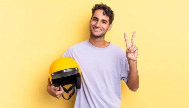 İspanyol yakışıklı adam gülümsüyor ve mutlu görünüyor, zafer ya da barış işareti yapıyor. Motosiklet kaskı konsepti