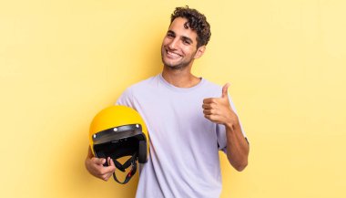 İspanyol yakışıklı adam kendini gururlu hissediyor, başparmağıyla olumlu gülümsüyor. Motosiklet kaskı konsepti