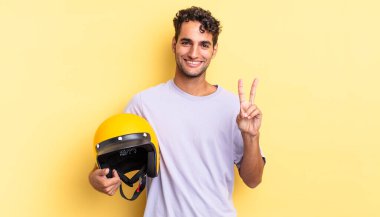 İspanyol yakışıklı adam gülümsüyor ve arkadaş canlısı görünüyor, iki numarayı gösteriyor. Motosiklet kaskı konsepti