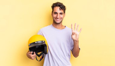 İspanyol yakışıklı adam gülümsüyor ve arkadaş canlısı görünüyor, dört numarayı gösteriyor. Motosiklet kaskı konsepti