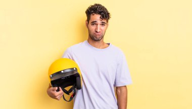 Hispanik yakışıklı adam üzgün ve mızmız, mutsuz bir bakışla ağlıyor. Motosiklet kaskı konsepti