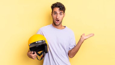 İspanyol yakışıklı adam şaşırmış ve şok olmuş görünüyor. Çenesi düşmüş ve elinde bir nesne var. Motosiklet kaskı konsepti