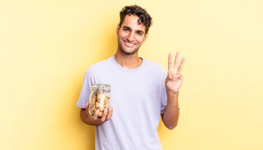 İspanyol yakışıklı adam gülümsüyor ve arkadaş canlısı görünüyor, üç numarayı gösteriyor. kurabiye konsepti