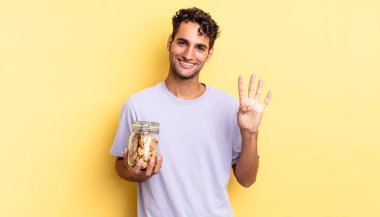 İspanyol yakışıklı adam gülümsüyor ve arkadaş canlısı görünüyor, dört numarayı gösteriyor. kurabiye konsepti