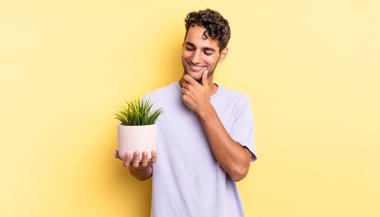 Mutlu, kendine güvenen, elleri çenesinde gülümseyen İspanyol yakışıklı bir adam. dekoratif bitki konsepti