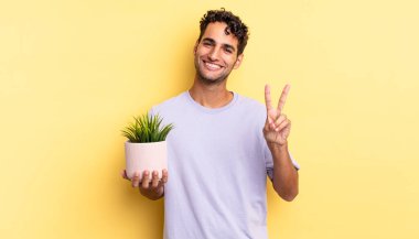 İspanyol yakışıklı adam gülümsüyor ve mutlu görünüyor, zafer ya da barış işareti yapıyor. dekoratif bitki konsepti