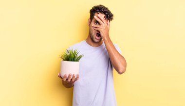 İspanyol yakışıklı adam şok olmuş, korkmuş ya da korkmuş görünüyor. Yüzü elle kapatılmış. dekoratif bitki konsepti
