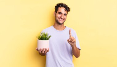 Hispanik yakışıklı adam gururla gülümsüyor ve kendinden emin bir numara oluyor. dekoratif bitki konsepti