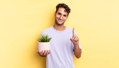 İspanyol yakışıklı adam gülümsüyor ve arkadaş canlısı görünüyor, bir numarayı gösteriyor. dekoratif bitki konsepti