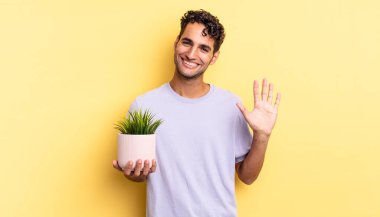 İspanyol yakışıklı adam mutlu bir şekilde gülümsüyor, el sallıyor, seni selamlıyor ve selamlıyor. dekoratif bitki konsepti