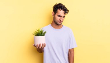 Hispanik yakışıklı adam üzgün, üzgün ya da kızgın hissediyor ve yana bakıyor. dekoratif bitki konsepti