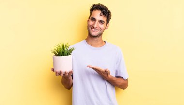 İspanyol yakışıklı adam neşeyle gülümsüyor, mutlu hissediyor ve bir konsept gösteriyor. dekoratif bitki konsepti