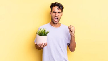 İspanyol yakışıklı adam sinirli bir ifadeyle agresif bir şekilde bağırıyor. dekoratif bitki konsepti