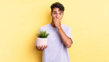 İspanyol yakışıklı adam şok olmuş bir şekilde ağzını kapatıyor. dekoratif bitki konsepti