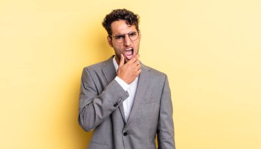 Ağzı ve gözleri açık, eli çenesinde İspanyol yakışıklı bir adam. iş kavramı