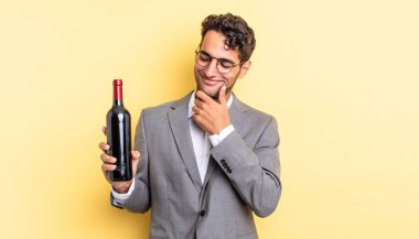 Mutlu, kendine güvenen, elleri çenesinde gülümseyen İspanyol yakışıklı bir adam. şarap şişesi konsepti