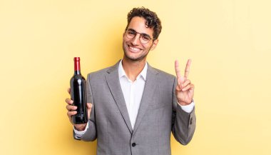 İspanyol yakışıklı adam gülümsüyor ve mutlu görünüyor, zafer ya da barış işareti yapıyor. şarap şişesi konsepti