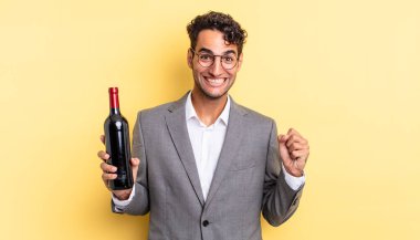 İspanyol yakışıklı adam şokta, gülüyor ve başarıyı kutluyor. şarap şişesi konsepti