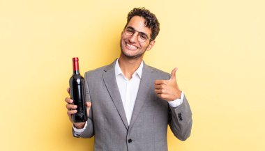 İspanyol yakışıklı adam kendini gururlu hissediyor, başparmağıyla olumlu gülümsüyor. şarap şişesi konsepti
