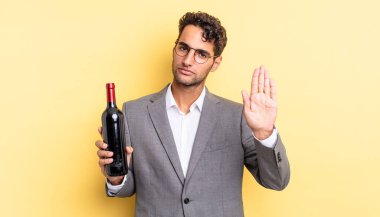 İspanyol yakışıklı adam ciddi görünüyor. Avuç içi gösteriyor. Durdurma hareketi yapıyor. şarap şişesi konsepti