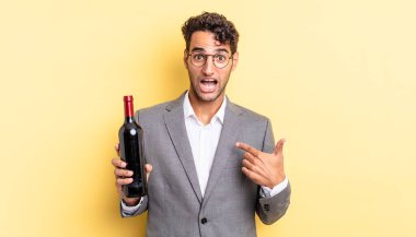 İspanyol yakışıklı adam mutlu hissediyor ve heyecanla kendini işaret ediyor. şarap şişesi konsepti