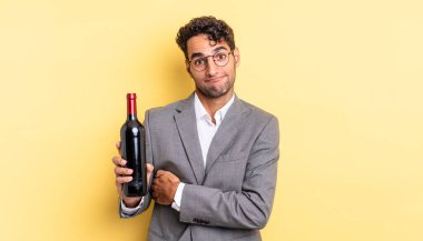 İspanyol yakışıklı adam omuz silkiyor, kafası karışık ve kararsız. şarap şişesi konsepti