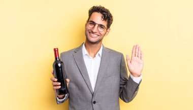 İspanyol yakışıklı adam mutlu bir şekilde gülümsüyor, el sallıyor, seni selamlıyor ve selamlıyor. şarap şişesi konsepti