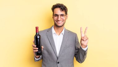 İspanyol yakışıklı adam gülümsüyor ve arkadaş canlısı görünüyor, iki numarayı gösteriyor. şarap şişesi konsepti