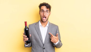 İspanyol yakışıklı adam şok olmuş ve ağzı açık, kendini işaret ederek şaşırmış görünüyor. şarap şişesi konsepti