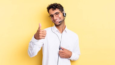 İspanyol yakışıklı adam kendini gururlu hissediyor, başparmağıyla olumlu gülümsüyor. tele pazarlamacı konsepti