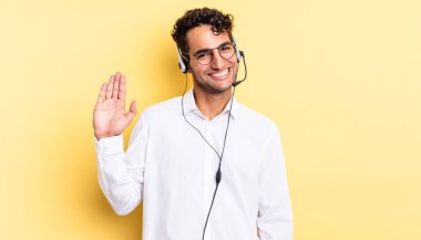 İspanyol yakışıklı adam mutlu bir şekilde gülümsüyor, el sallıyor, seni selamlıyor ve selamlıyor. tele pazarlamacı konsepti