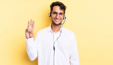 İspanyol yakışıklı adam gülümsüyor ve arkadaş canlısı görünüyor, üç numarayı gösteriyor. tele pazarlamacı konsepti