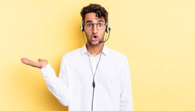 İspanyol yakışıklı adam şaşırmış ve şok olmuş görünüyor. Çenesi düşmüş ve elinde bir nesne var. tele pazarlamacı konsepti