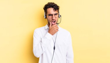 Ağzı ve gözleri açık, eli çenesinde İspanyol yakışıklı bir adam. tele pazarlamacı konsepti