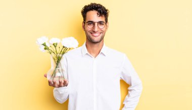 İspanyol yakışıklı adam mutlu bir şekilde gülümsüyor, eli kalçasında ve kendinden emin. çiçek saksı konsepti