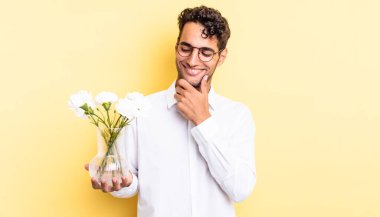 Mutlu, kendine güvenen, elleri çenesinde gülümseyen İspanyol yakışıklı bir adam. çiçek saksı konsepti