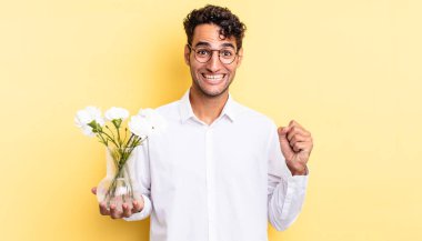 İspanyol yakışıklı adam şokta, gülüyor ve başarıyı kutluyor. çiçek saksı konsepti