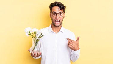 İspanyol yakışıklı adam mutlu hissediyor ve heyecanla kendini işaret ediyor. çiçek saksı konsepti