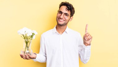 İspanyol yakışıklı adam gülümsüyor ve arkadaş canlısı görünüyor, bir numarayı gösteriyor. çiçek saksı konsepti