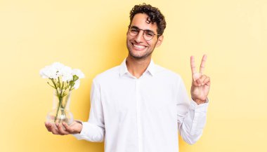 İspanyol yakışıklı adam gülümsüyor ve arkadaş canlısı görünüyor, iki numarayı gösteriyor. çiçek saksı konsepti