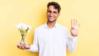 İspanyol yakışıklı adam gülümsüyor ve arkadaş canlısı görünüyor, dört numarayı gösteriyor. çiçek saksı konsepti
