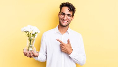 İspanyol yakışıklı adam neşeyle gülümsüyor, mutlu hissediyor ve bir tarafı işaret ediyor. çiçek saksı konsepti