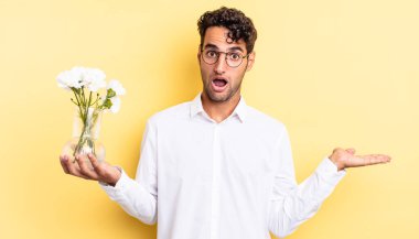 İspanyol yakışıklı adam şaşırmış ve şok olmuş görünüyor. Çenesi düşmüş ve elinde bir nesne var. çiçek saksı konsepti