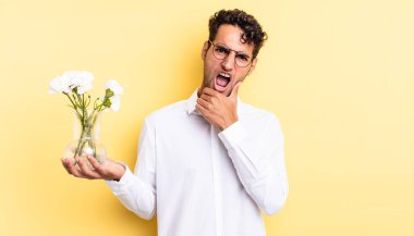 Ağzı ve gözleri açık, eli çenesinde İspanyol yakışıklı bir adam. çiçek saksı konsepti