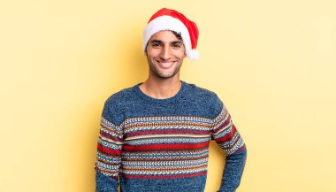 İspanyol yakışıklı adam mutlu bir şekilde gülümsüyor, eli kalçasında ve kendinden emin. Noel konsepti
